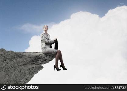 Young businesswoman with suitcase sitting on rock edge. Taking break from office
