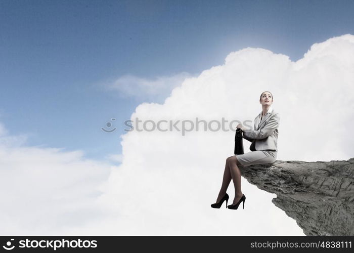 Young businesswoman with suitcase sitting on rock edge. Taking break from office