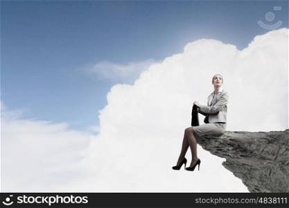Young businesswoman with suitcase sitting on rock edge. Taking break from office