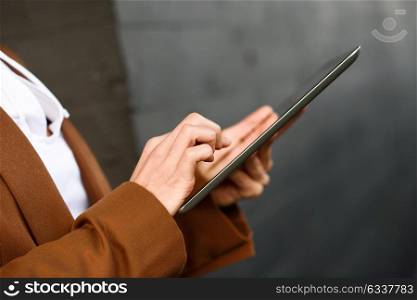 Young businesswoman with tablet computer standing outside of an office building. Beautiful woman wearing formal wear. Young girl with brown jacket.