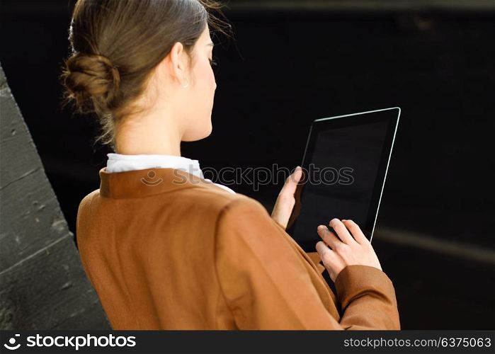 Young businesswoman with tablet computer standing outside of an office building. Beautiful woman wearing formal wear. Young girl with brown jacket.