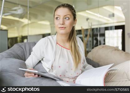 Young businesswoman with tablet PC and book looking away in office