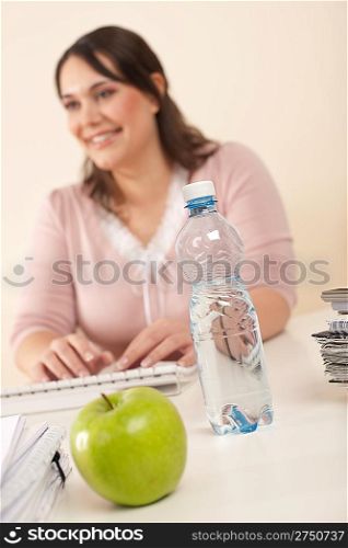Young businesswoman working at office, focus on apple and bottle of water on table