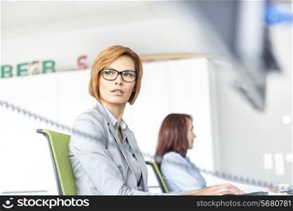 Young businesswoman working on computer with colleague in background at office