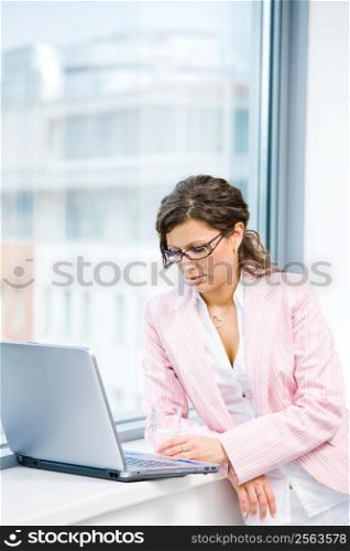 Young businesswoman working on laptop computer at office window.