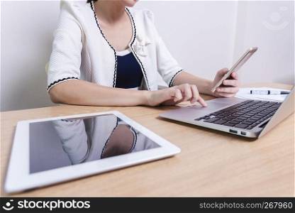 Young businesswoman working with laptop, mobile and tablet in office. Business and technology concept.