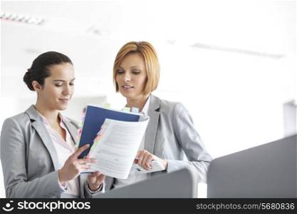 Young businesswomen discussing over book in office