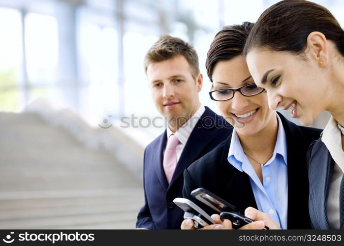 Young businesswomen sharing info on mobile phones. Selective focus is placed on the woman in the middle.