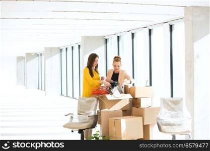 Young businesswomen untangling cords while standing by cardboard boxes in office