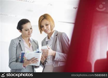 Young businesswomen with book while using cell phone in office