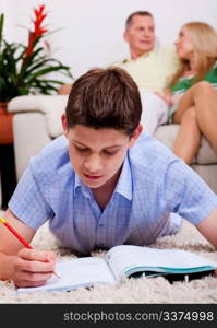 Young buy busy with his books and study material lying on carpet with family in the background