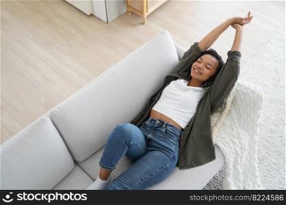 Young calm mixed race woman relaxing lying on comfortable sofa in living room, lazy happy african american young female rests on couch, enjoying peace of mind, stretching body after day sleep.. Young calm mixed race girl relaxing lying on comfortable sofa, stretching body after day sleep