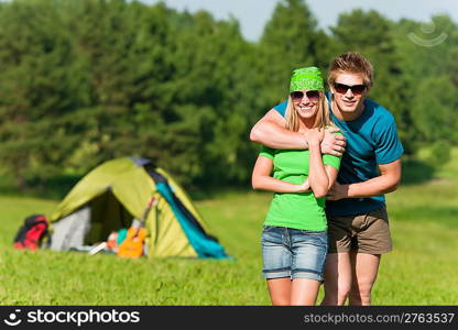 Young camping couple hugging in summer countryside tent in background