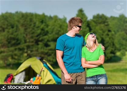 Young camping couple hugging in summer countryside tent in background