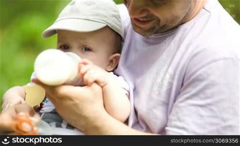 Young caring father feeding his baby son from the bottle outdoor