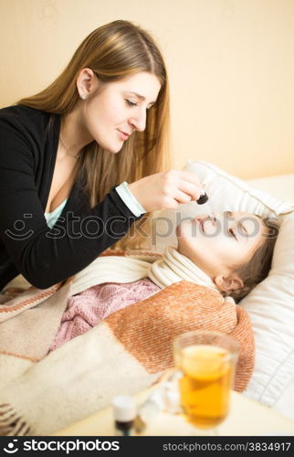 Young caring mother spraying daughters nose lying in bed