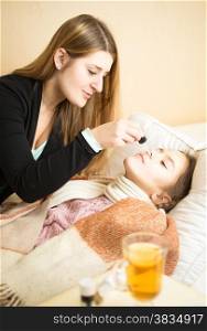 Young caring mother spraying daughters nose lying in bed