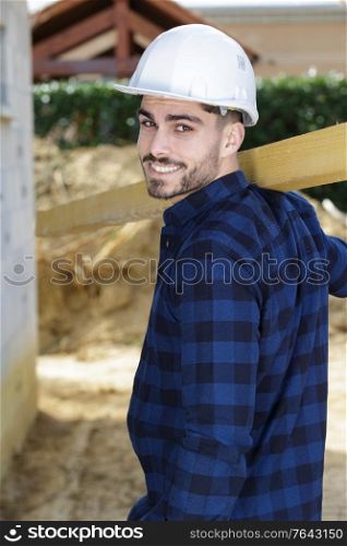 young carpenter carrying length of wood