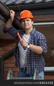 Young carpenter in hardhat examining house roof