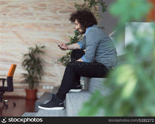 Young casual businessman holding smartphone in the startup office