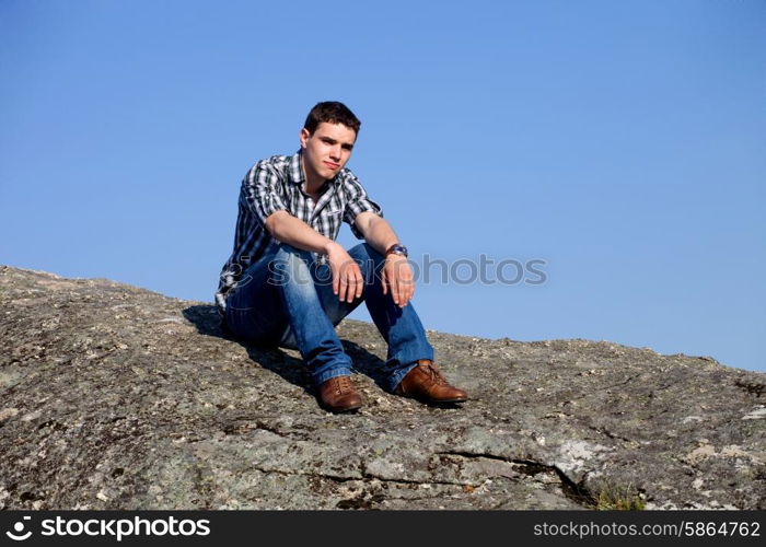 young casual man on top of a rock with the sky as background