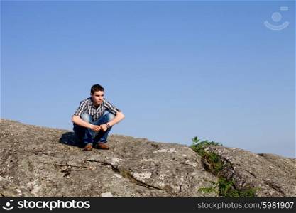 young casual man on top of a rock with the sky as background