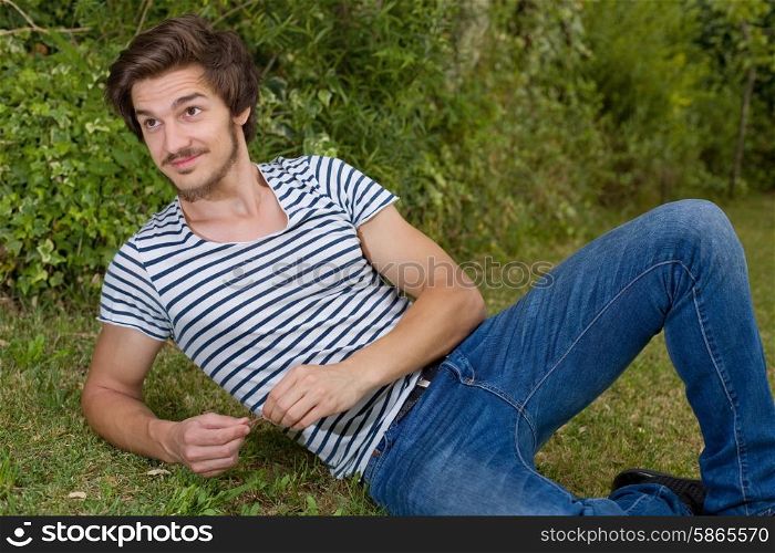 young casual man posing seated, smiling at the camera, outdoors