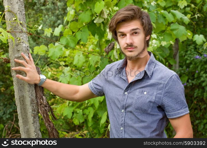 young casual man posing seated, smiling at the camera, outdoors