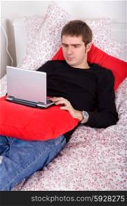young casual man working with computer in bed