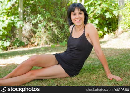 young casual woman posing seated, smiling at the camera, outdoors