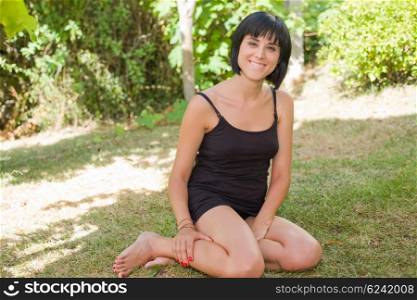 young casual woman posing seated, smiling at the camera, outdoors