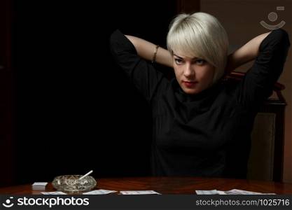young Caucasian blonde woman sitting at a table and undressing after losing at cards