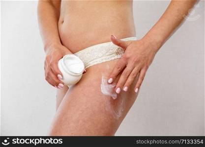 young Caucasian brunette woman in light lingerie applies cream to legs and buttocks