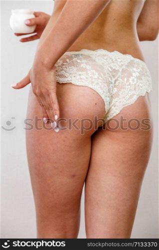 young Caucasian brunette woman in light lingerie applies cream to legs and buttocks