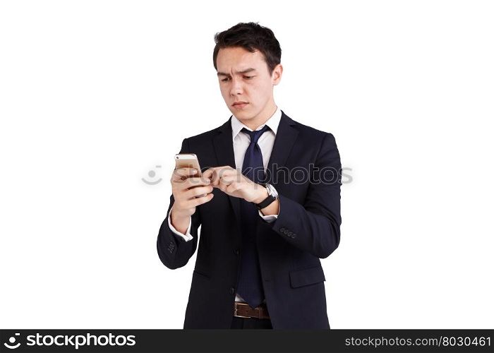 Young Caucasian business man frowning looking at mobile phone. A young Caucasian business man is frowning holding a moble phone. He is operating the smart phone with fingers on the screen.