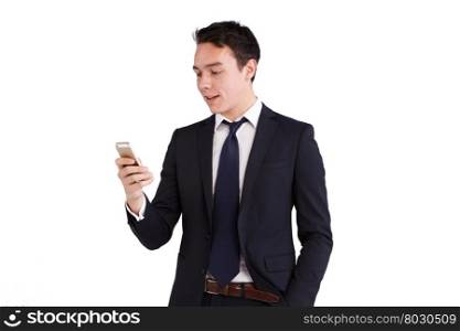 Young Caucasian business man looking at mobile phone smiling. A young Caucasian business man is holding a mobile phone smiling. His hand is on the screen operating the smart phone. He is looking at the smart phone with one hand in the pocket.