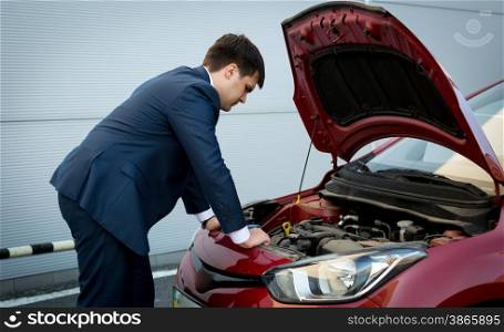 Young caucasian businessman trying to fix crashed down car engine
