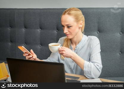 Young caucasian businesswoman with smartphone and cup of coffee working at home office. Businesswoman with smartphone and cup of coffee