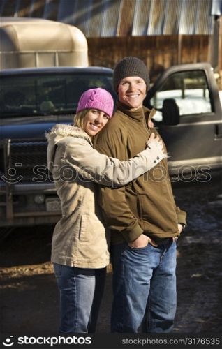 Young Caucasian couple embracing with truck in background.