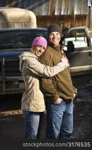 Young Caucasian couple embracing with truck in background.
