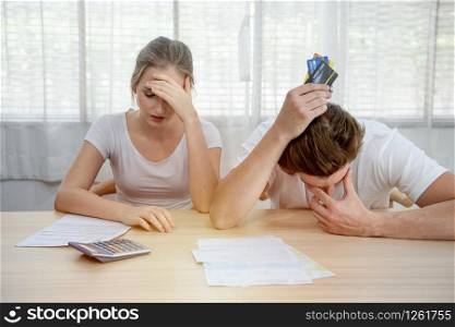 Young caucasian couple hand holding credit card and debt bill on table in home,men and women have overdue financial foreclosure problem sit in room with serious and unhappy payment.