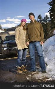 Young Caucasian couple holding hands looking at viewer with truck in background.