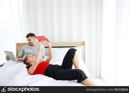 Young Caucasian couple love relaxing with laptop and tablet in social media for shopping online in bedroom. Technology for Married family lifestyle on holiday Concept.