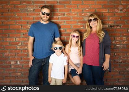 Young Caucasian Family Wearing Sunglasses Against Brick Wall.