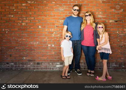 Young Caucasian Family Wearing Sunglasses Against Brick Wall.