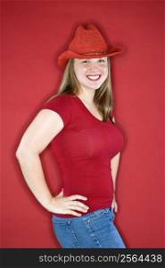 Young Caucasian female adult in red cowboy hat on red background.