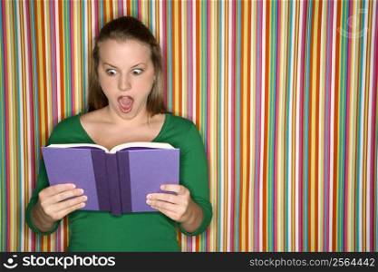 Young Caucasian female adult reading book making expression.