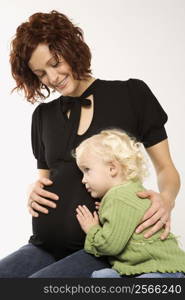 Young Caucasian female child with ear against her mother&acute;s pregnant belly.