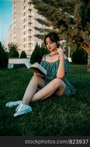 young caucasian girl in vintage retro dress reads a book on the lawn during sunset