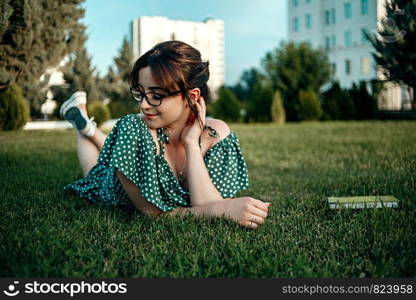 young caucasian girl in vintage retro dress reads a book on the lawn during sunset